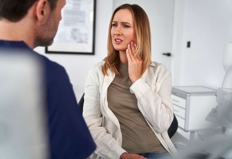 A woman holding her jaw in pain during consultation for TMJ in a dental clinic in Terre Haute, IN